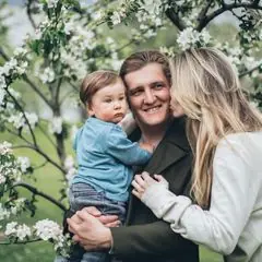 Casal com bebê sorrindo sob árvores floridas