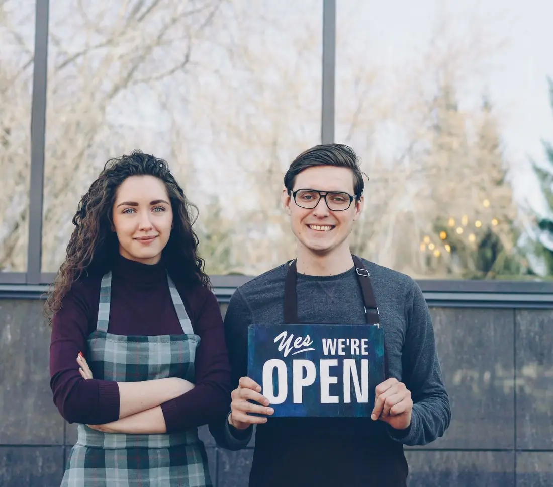 Casal de empreendedores segurando placa de aberto na porta da loja