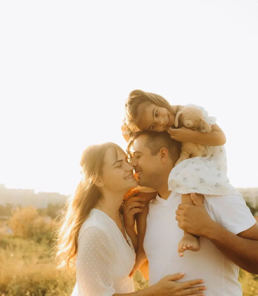 Pai e mãe abraçando a filha pequena ao pôr do sol